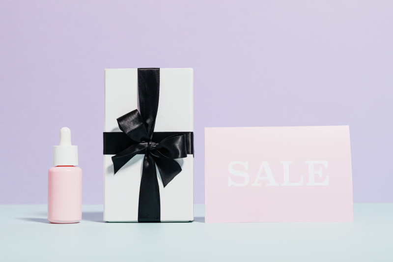 A gift box with a ribbon beside a serum bottle and a small jar.