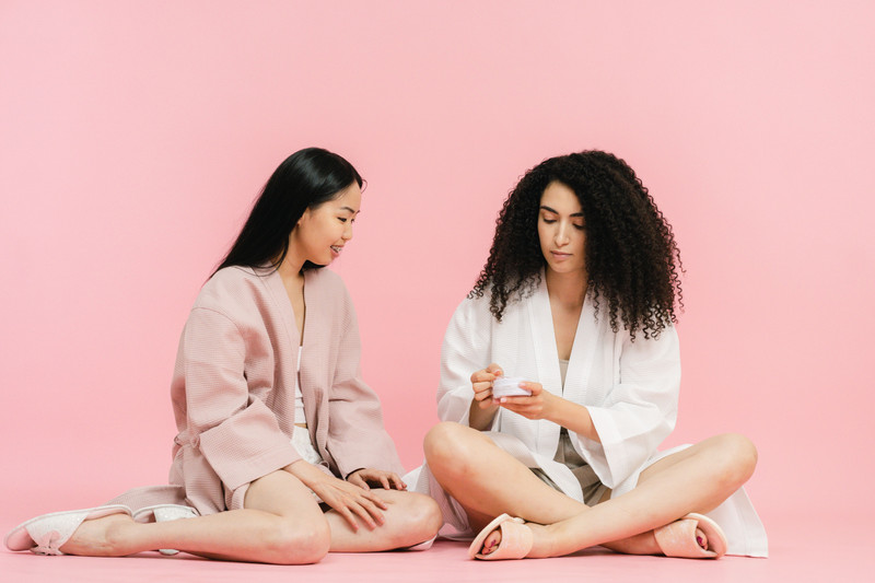 Two women in robes sitting on a pink floor, laughing.